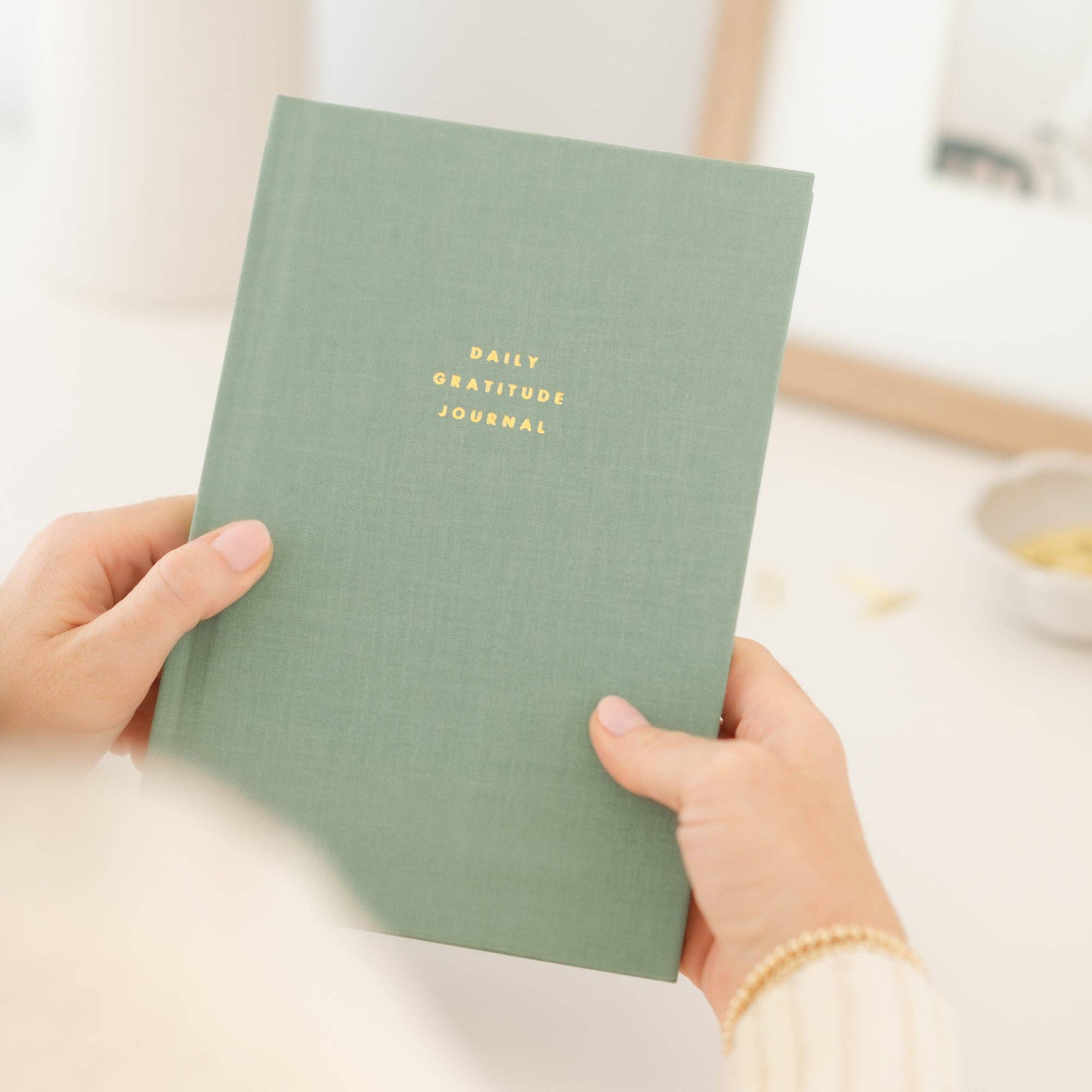 Hands holding Daily gratitude journal with hardcover binding and "DAILY GRATITUDE JOURNAL" text.