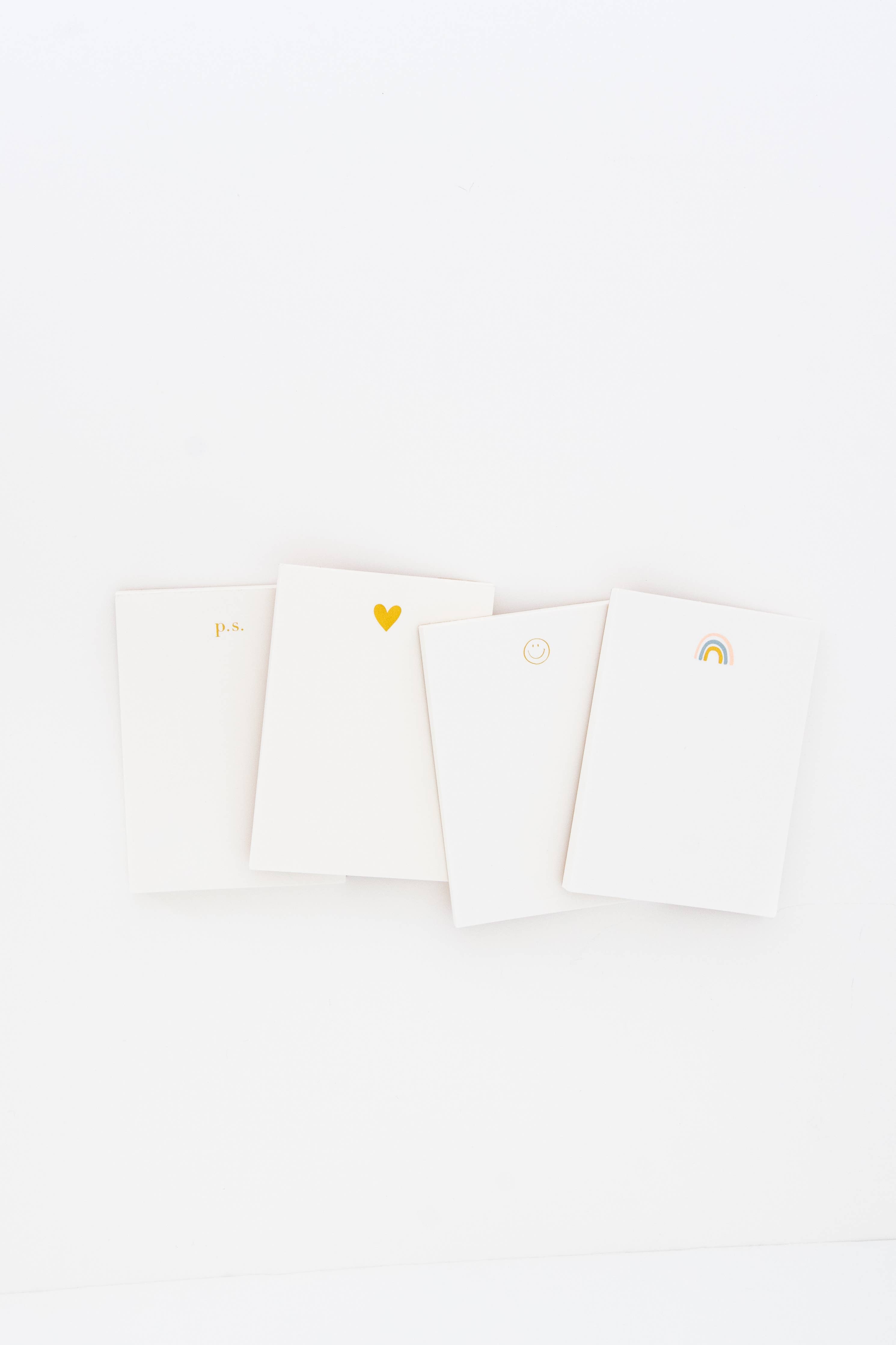 Stack of miniature notebooks with p.s, gold heart, smiley face and rainbow design on top notebook.