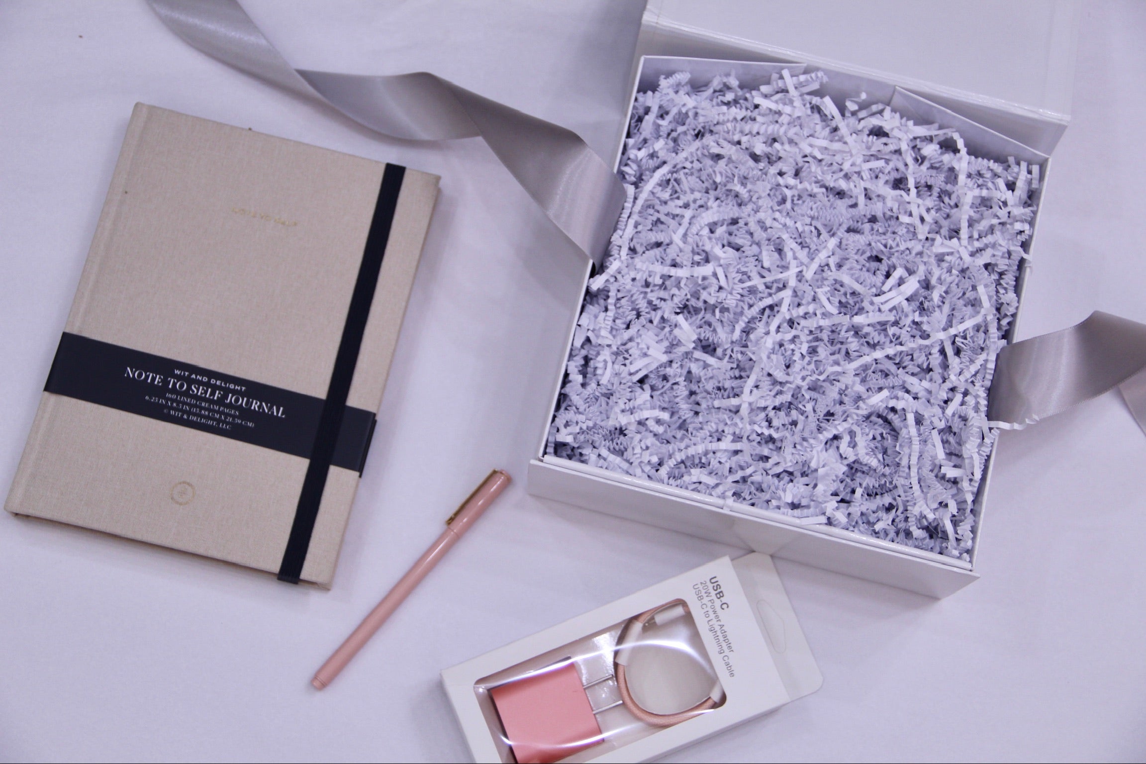 Cream lined journal, rose pen, pink charger in its box, open box filled with crinkle paper
