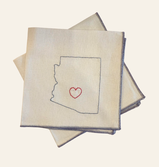 Folded cocktail napkin with Arizona outline and heart embroidered on a light background