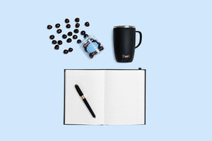 open lined notepad, black pen, black tumbler, open candy jar with candy outside