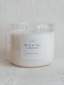 White candle in a glass jar with a label on a textured white surface