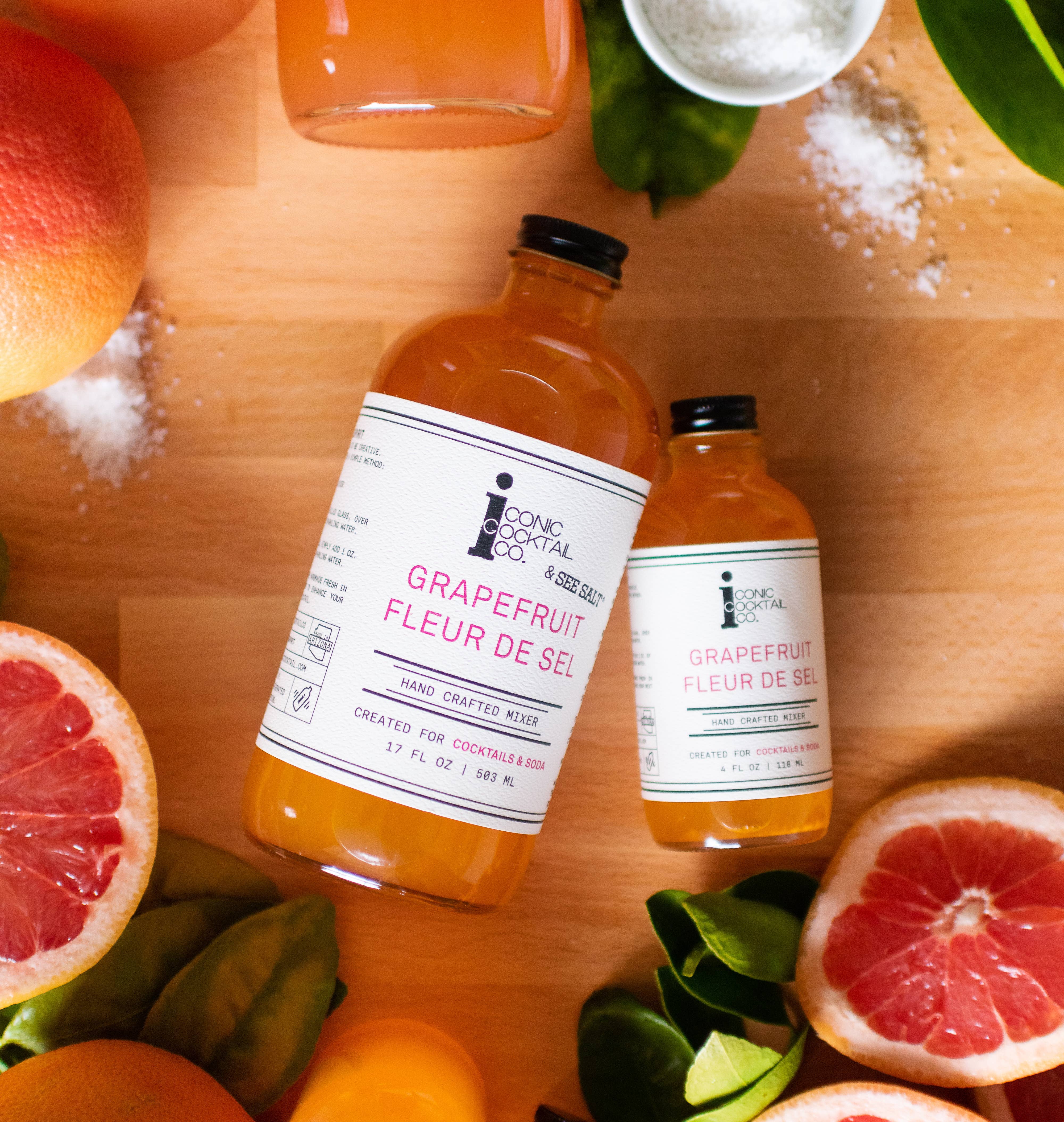 Two bottles of Grapefruit Fleur de Sel on a wooden surface with grapefruits and salt crystals.