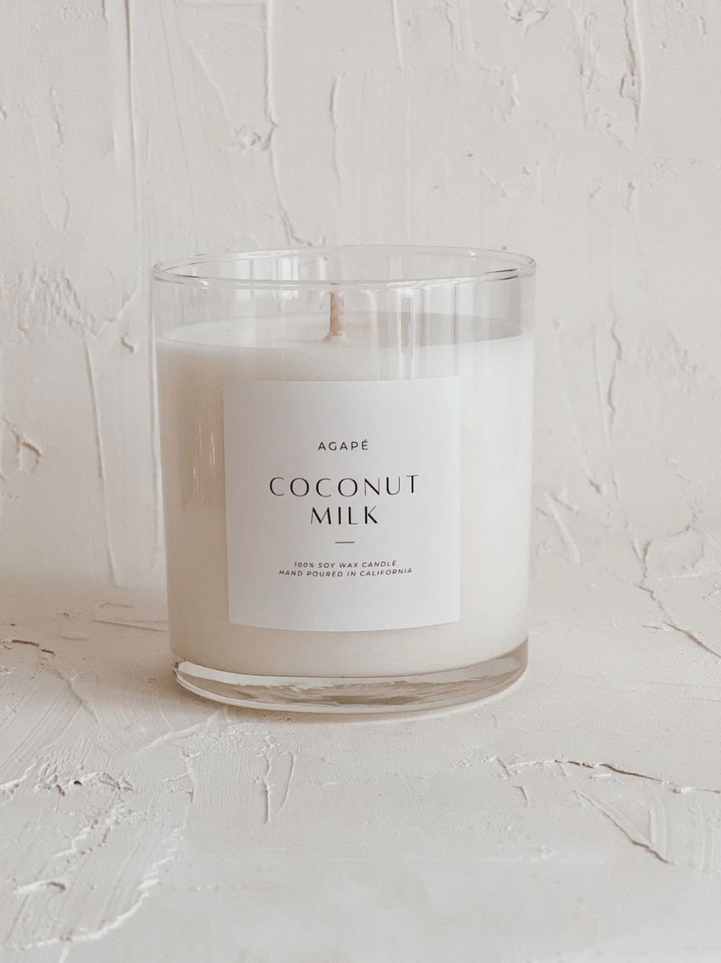 A single-wick soy candle with a clear glass jar, labeled 'Coconut Milk' with a white and green label design, on a white background.